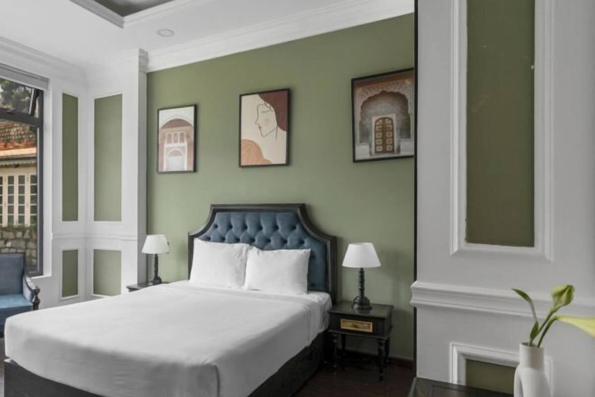 A hotel room with a large bed, two bedside tables with lamps, a window with a view of a building, and three framed pictures on the wall.