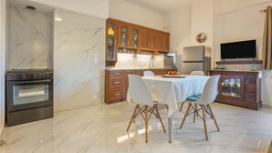 A modern kitchen with marble flooring, wooden cabinets, a dining table with chairs, and a TV mounted on the wall.