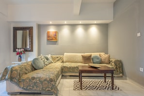 A living room with a sectional sofa, a coffee table, a patterned rug, a vase with flowers, and a painting on the wall.