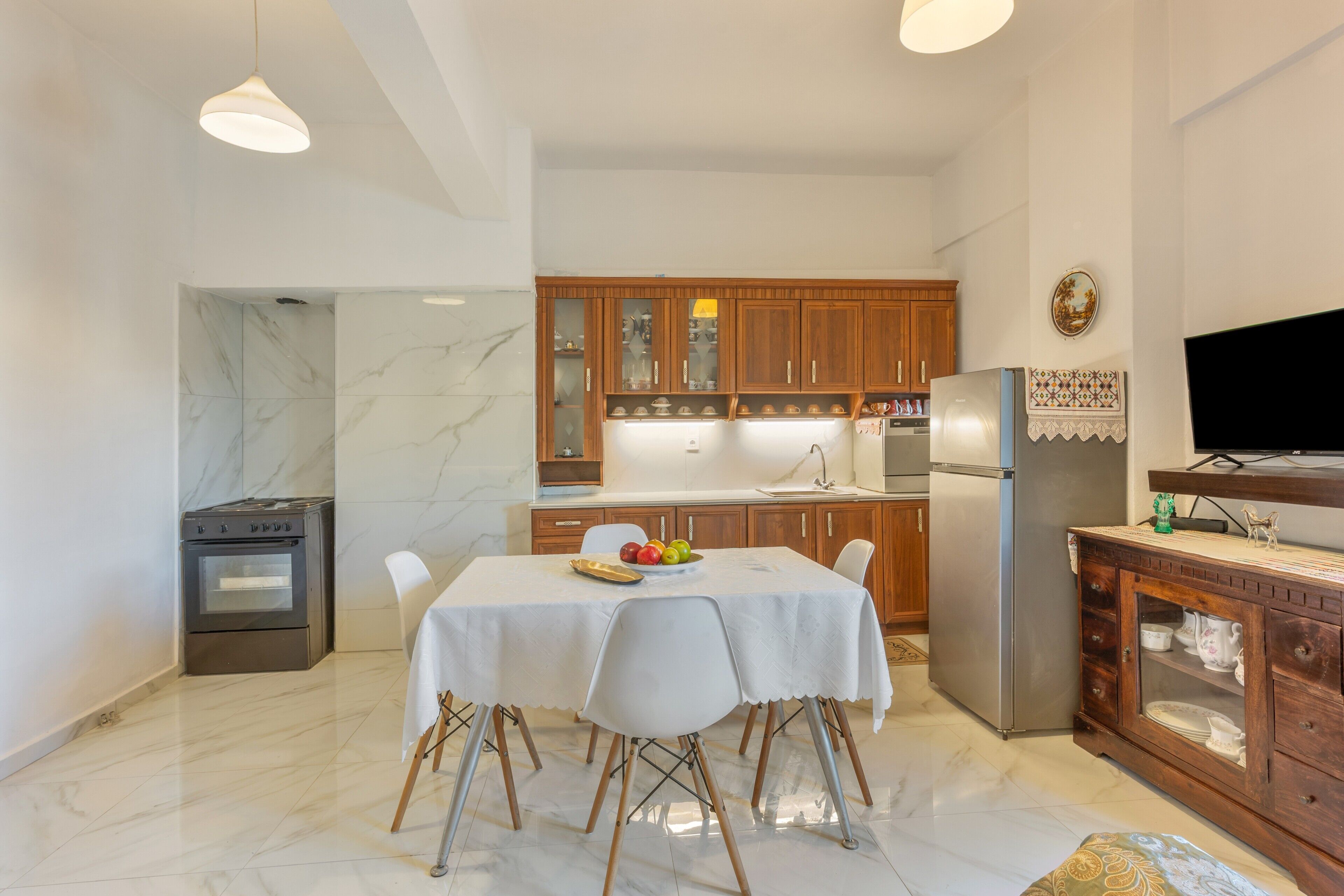 A modern kitchen with marble flooring, wooden cabinets, a dining table with chairs, and a built-in TV.