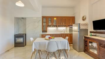 A modern kitchen with marble flooring, wooden cabinets, a dining table with chairs, and a built-in TV.