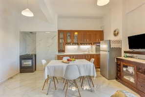 A modern kitchen with marble flooring, wooden cabinets, a dining table with chairs, and a built-in TV.