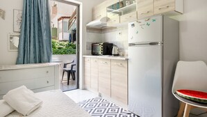 A compact kitchen with a microwave, toaster, and refrigerator, a bed with a patterned rug, and a chair with a watermelon slice.
