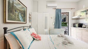 A bedroom with a bed, a painting, a wardrobe, a bathroom, and a kitchenette.