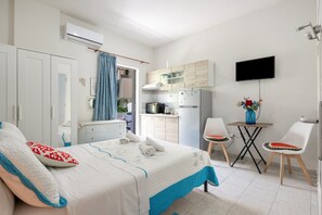 Un dormitorio con cama, escritorio, silla, televisión y kitchenette.