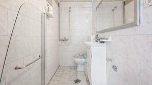 A bathroom with white tiles, a shower, a toilet, and a sink.