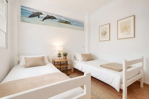 Un dormitorio con dos camas individuales, una mesita de noche con lámpara, un cuadro de delfines en la pared y estrellas de mar enmarcadas.