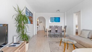 A modern living room with a TV, seating area, dining table, and a large plant. - Apartment 'Beach Front Sea View Punta Prima' with Sea View, Wi-Fi and Air Conditioning (Torrevieja)