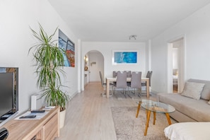 A modern living room with a TV, seating area, dining table, and a large plant.