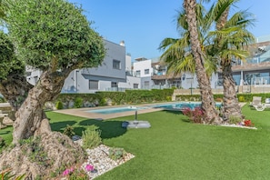 A modern building with a pool, surrounded by well-maintained grass and palm trees.