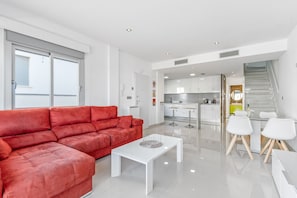 A modern living room with a red sofa, white coffee table, and a kitchen area with white cabinets and a staircase.
