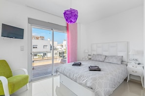A modern bedroom with a bed, a green chair, a TV, and a balcony view.