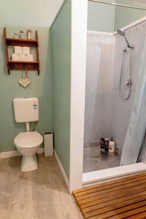 A bathroom with a toilet, a shower with a curtain, and shelves with toiletries. - Sleeps 4, Estuary Front in Pukehina Beach, two minutes to beach (Pukehina)