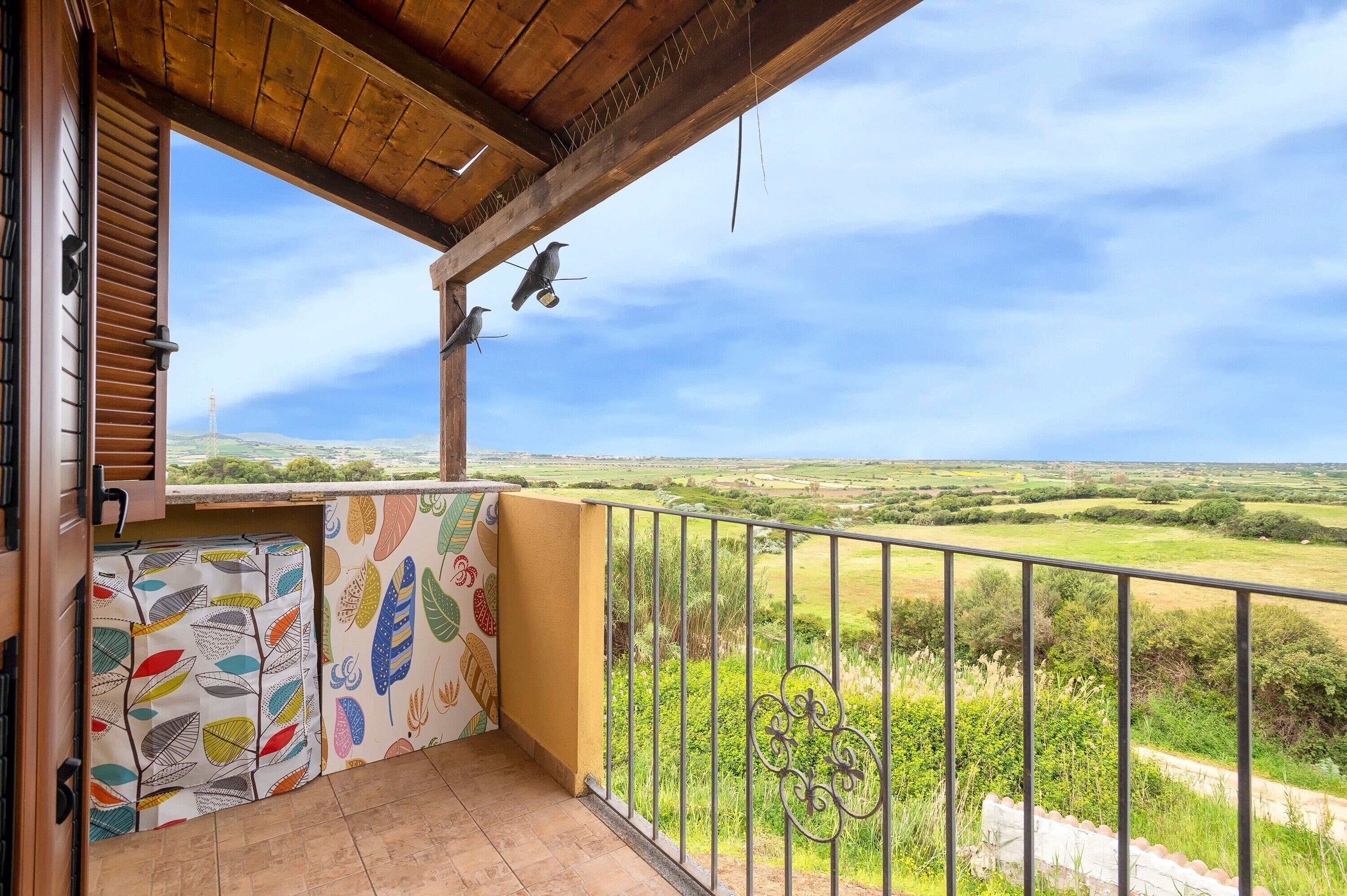 A balcony with a view of a green landscape, a railing, and a wooden ceiling.