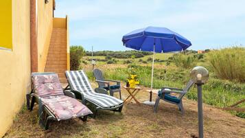 A patio with two lounge chairs, a blue umbrella, and a small table with a vase of flowers.