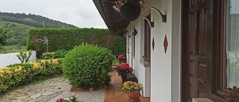 Una casa con porche de baldosas, plantas en macetas y vistas a un paisaje verde.