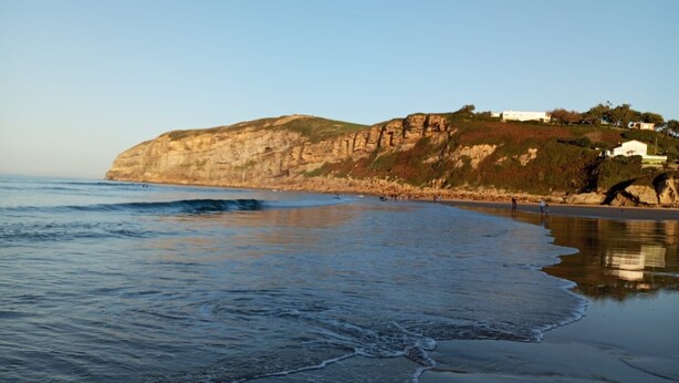 A coastal landscape with a cliff, beach, and buildings.