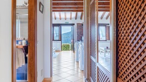A hallway leading to a balcony with a view of the outdoors, wooden beams, and a tiled floor.