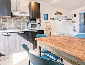 Une cuisine moderne équipée d’un four à micro-ondes, de meubles de rangement sombres et d’une table à manger en bois avec des chaises bleues.