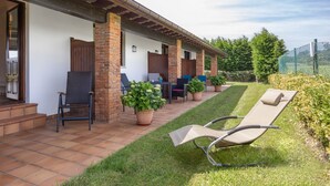 A covered patio with outdoor seating, a lounge chair, and potted plants.