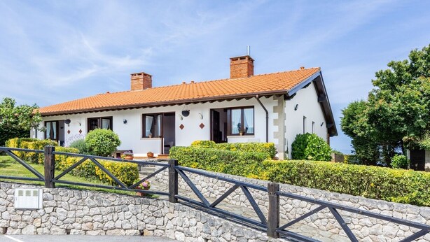 A two-story house with a stone wall entrance, a tiled roof, and a paved driveway.