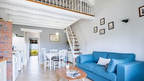 A spacious living area with a blue sofa, a dining table with chairs, a staircase, and a kitchen area with a brick column.