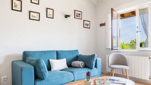 A blue sofa with pillows, a small round table with a magazine, and a chair.