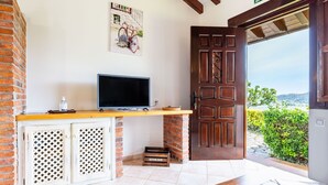 Um quarto com uma televisão sobre uma prateleira de madeira, uma porta que dá para o exterior e um cacto sobre uma mesa.