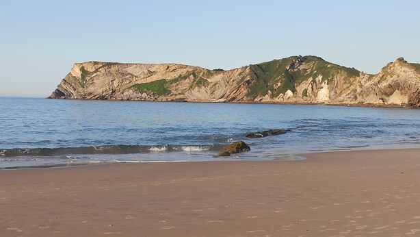 Uma praia com um penhasco rochoso ao fundo.