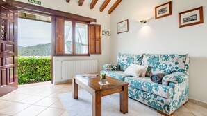 Quarto com teto de madeira, sofá estampado com motivos florais, mesa com um livro e vista para o verde lá fora.