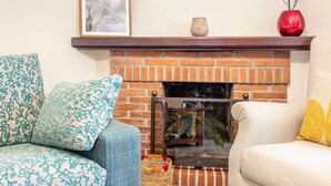Una sala de estar con chimenea de ladrillo, dos sofás estampados y una mesita con un jarrón.