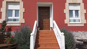Un edificio con fachada roja, una puerta de madera y una escalera que lleva a la entrada.