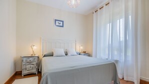 Un dormitorio con cama, mesitas de noche, una lámpara y cortinas de encaje.
