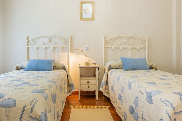 Quarto com duas camas, cada uma com cabeceira, mesa de cabeceira com abajur e uma pequena gaveta.