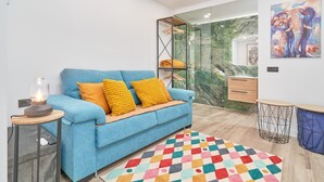 Ein modernes Wohnzimmer mit einem blauen Sofa, einem farbenfrohen Teppich, einer Glasdusche und einem Gemälde an der Wand.