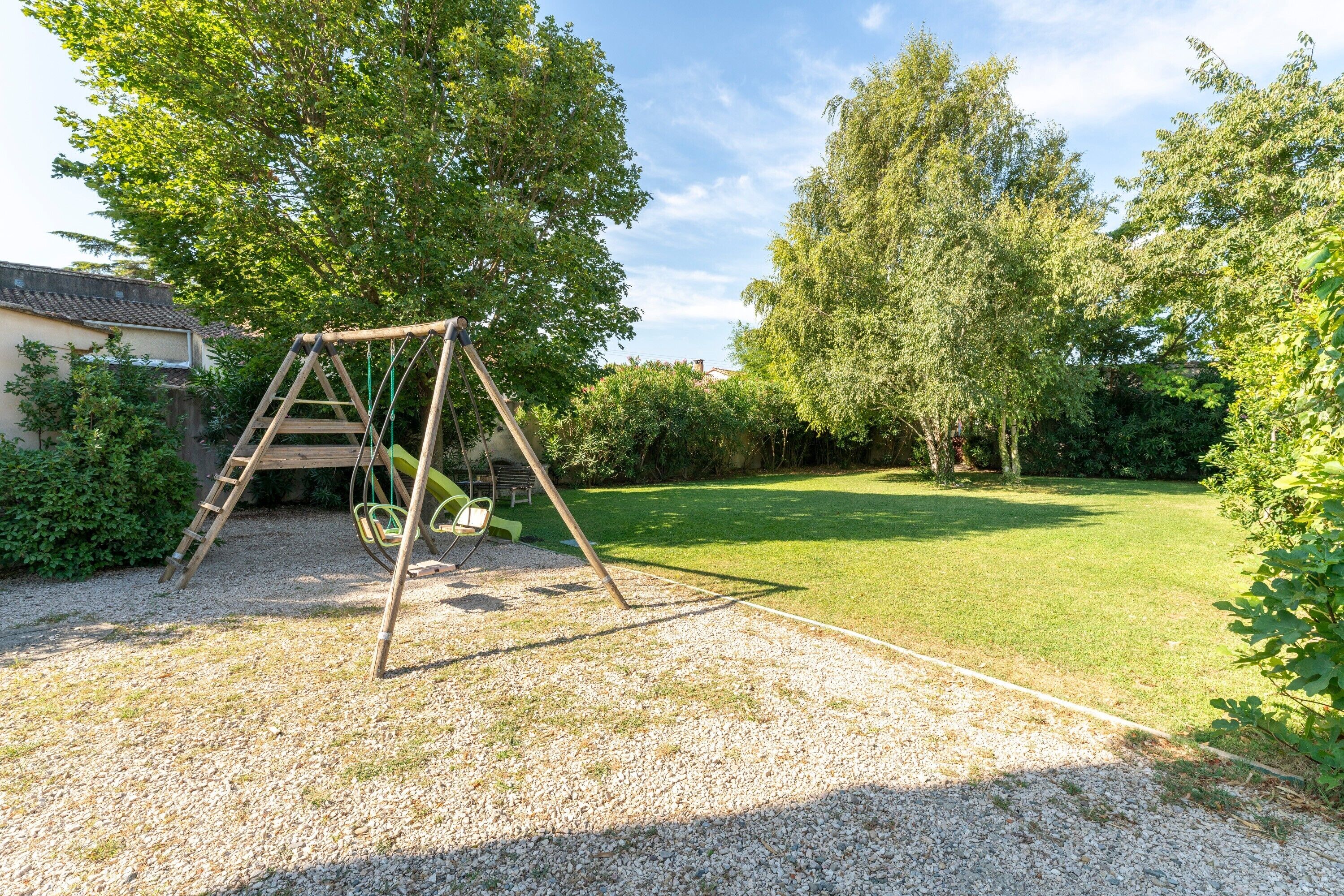 Un ensemble de balançoires en bois installé dans un jardin, avec une pelouse et des arbres.