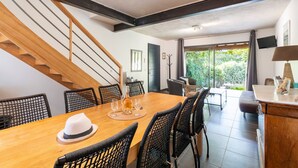A dining area with a wooden table, black wicker chairs, a white hat, and a bottle. - Holiday Home 'Grand Gîte De Tante Berthe' with Mountain View, Shared Pool and Wi-Fi (Camaret-sur-Aigues)