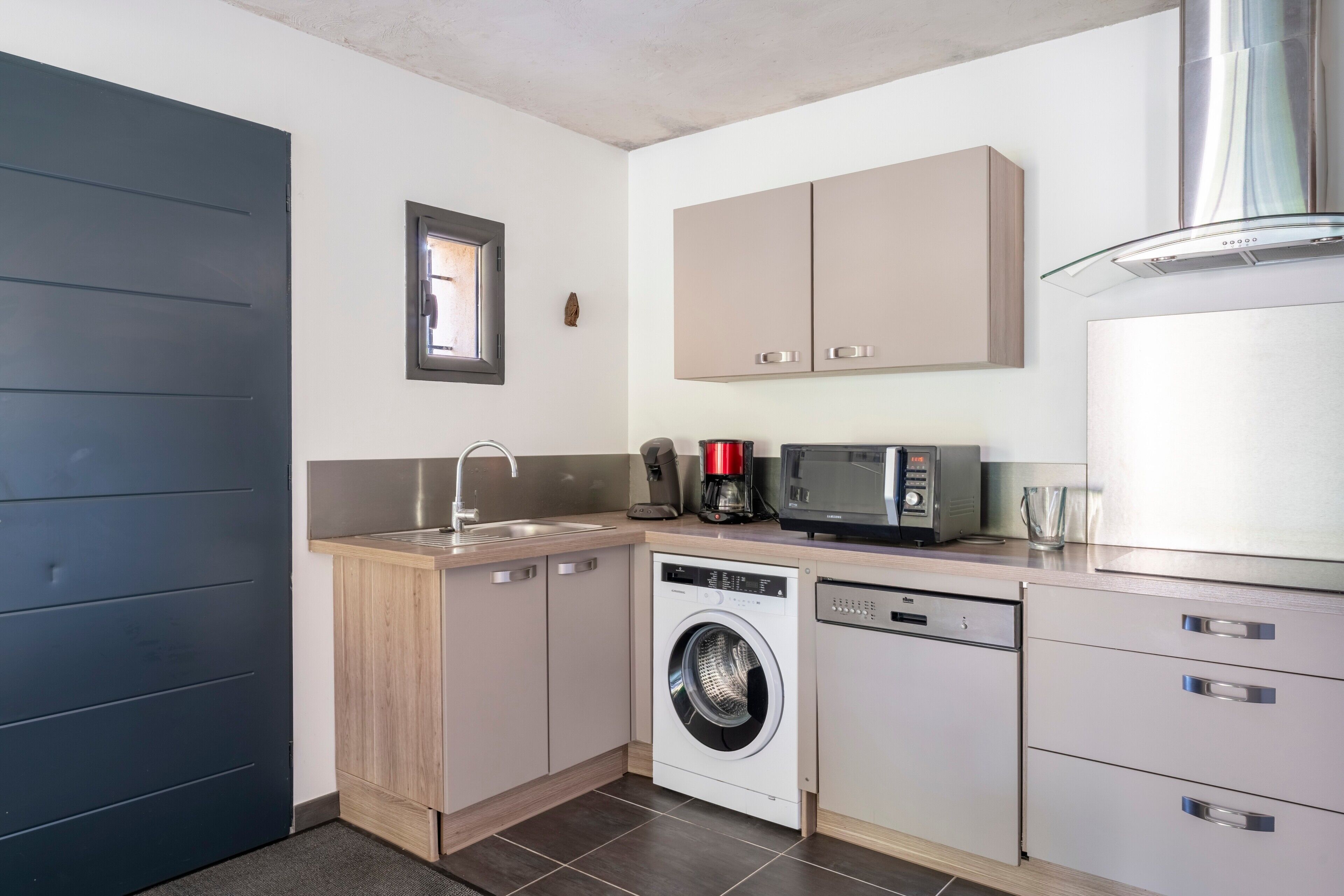 A compact kitchen with a washing machine, microwave, and a coffee maker.