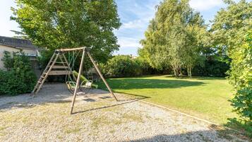 Un ensemble de balançoires en bois installé dans un jardin, avec une pelouse et des arbres.