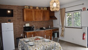 A kitchen with wooden cabinets, a white refrigerator, a dining table set for two, and a hanging light fixture. - Casa Trincadeira – Retreat with Private Jacuzzi Among Vineyards and Views of Palmela Castle (Palmela)