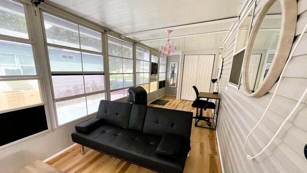 Ein modernes Wohnzimmer mit einer schwarzen Couch, Holzböden, großen Fenstern und einem Chandelier.
