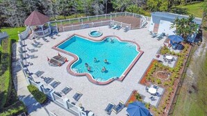 Ein Pool im Freien mit gewelltem Rand, umgeben von Liegestühlen und einer überdachten Sitzgruppe.