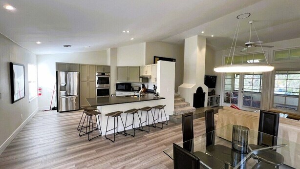 A modern kitchen with a central island, bar stools, and a dining area with a glass table.