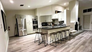 A modern kitchen with a central island, bar stools, stainless steel appliances, and a herringbone wood floor.
