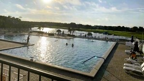 A swimming pool with multiple lanes, surrounded by lounge chairs and a view of a lake.