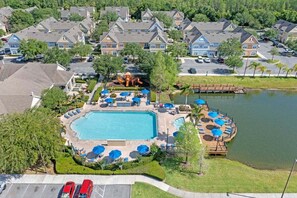 An aerial view of a residential area with a swimming pool, lounge chairs, and a dock over a lake.