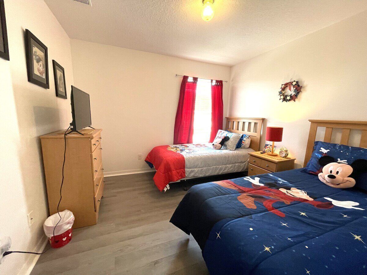 Une chambre avec deux lits, une commode, un bureau et un téléviseur fixé au mur.