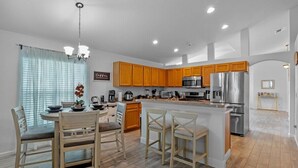 A modern kitchen with wooden cabinets, stainless steel appliances, and a central island with bar stools. - Wonderful Weston Hills Villa SE Facing Pool (Clermont)