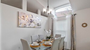 A dining area with a glass table, white chairs, and a chandelier. - Wonderful Weston Hills Villa SE Facing Pool (Clermont)