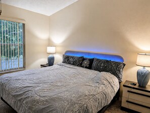 Ein Schlafzimmer mit einem Bett, einem Nachttisch, einer Lampe und einem Fenster.